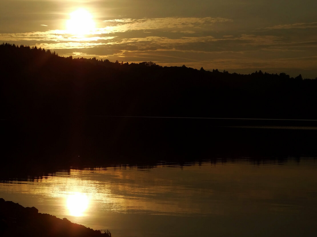 Ein See umgeben von Mergen im Hintergrund geht die Sonne unter