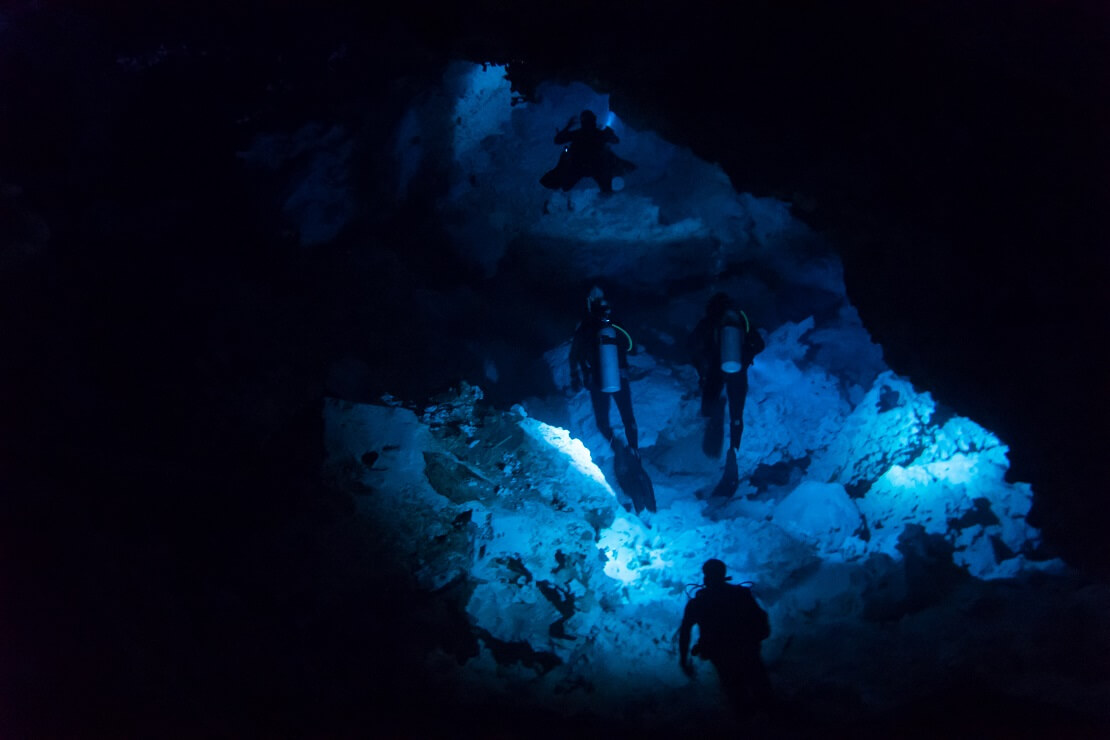 Drei Taucher tauchenin einer Dunkeln Höhle durch einen Tunnel