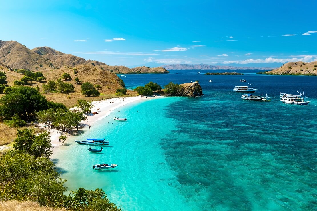 An der Küste von Komodo ist weißer Sand un türkis blaues Wasser und blauer Himmel