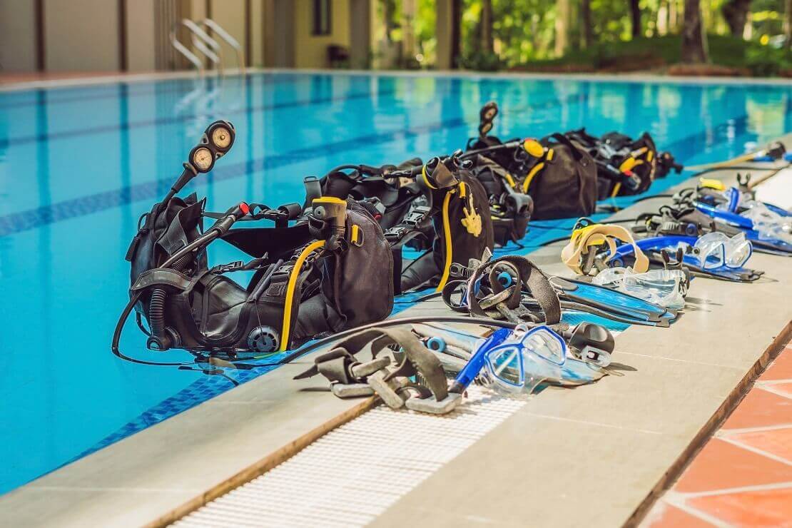 Viele Tauchausrüstungen liegen nebeneinander am Beckenrand eines Schwimmbeckens.