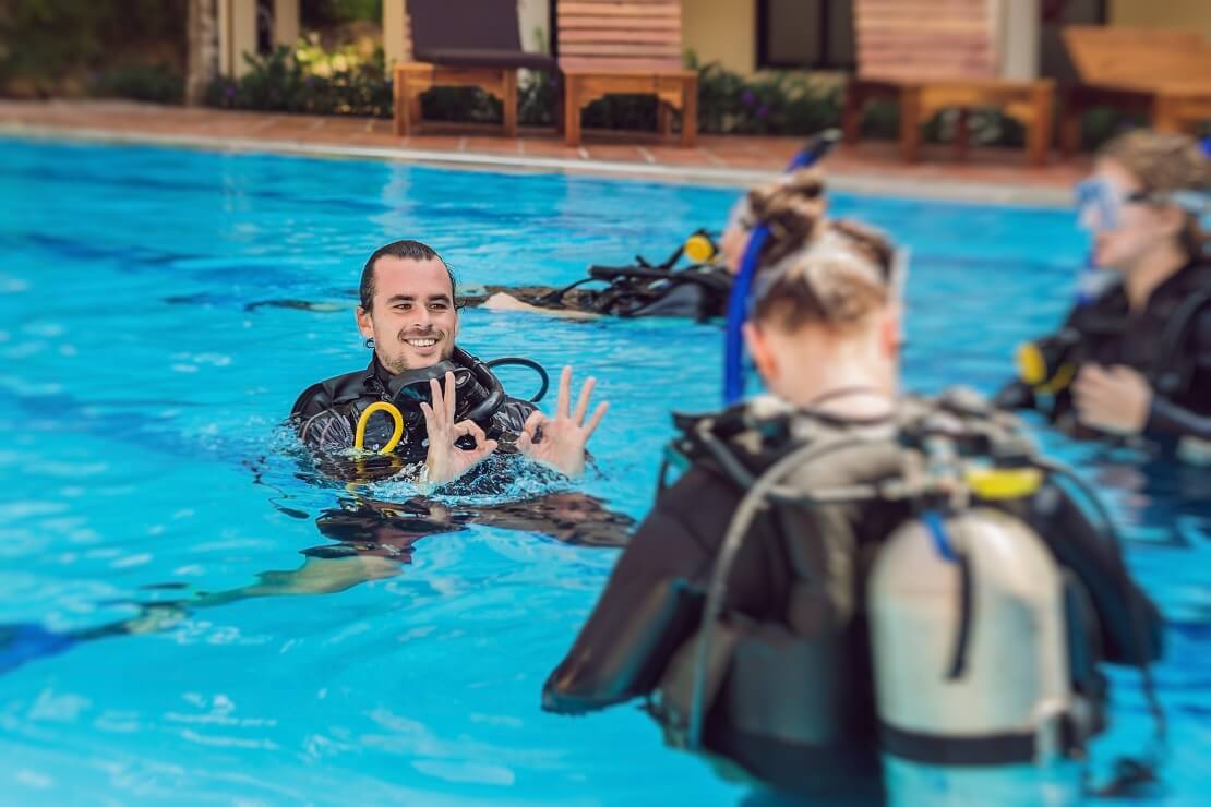 Taucher ist zu hälfte im Wasser und zeigt mit den Händen das alles okay ist