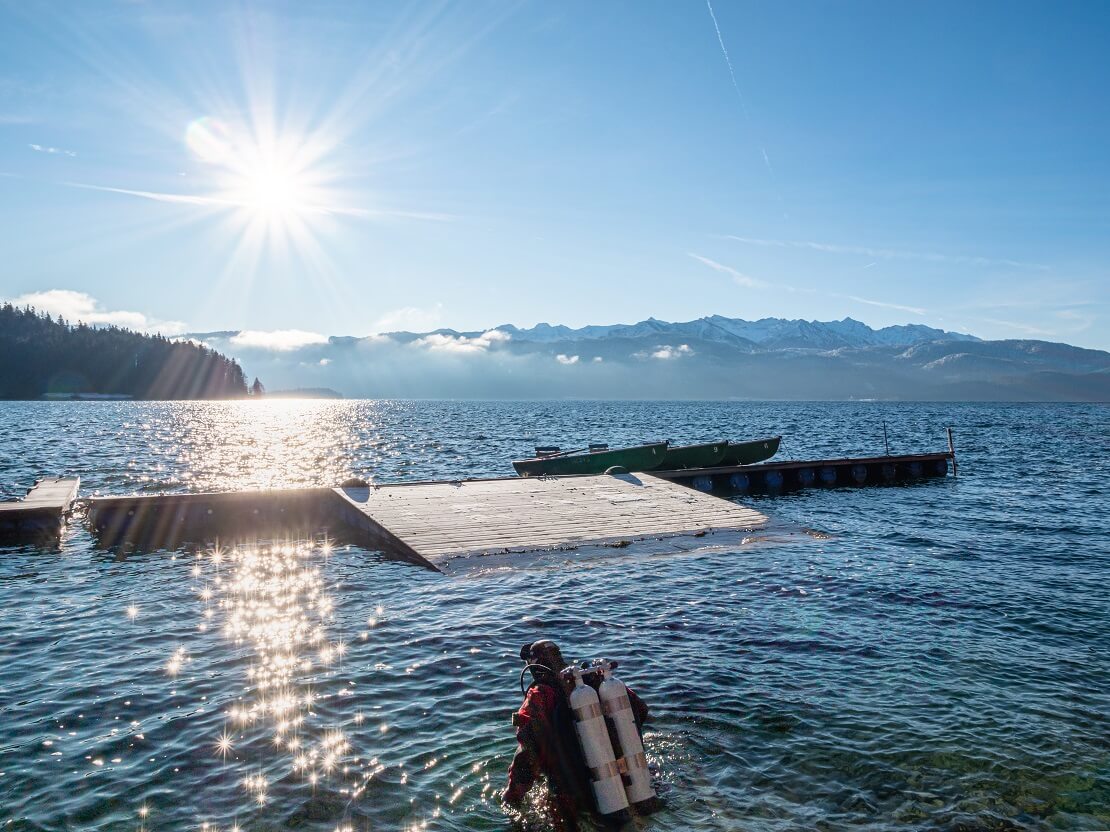 Taucher steigt mit Ausrüstung bei Sonnenschein in den See ein