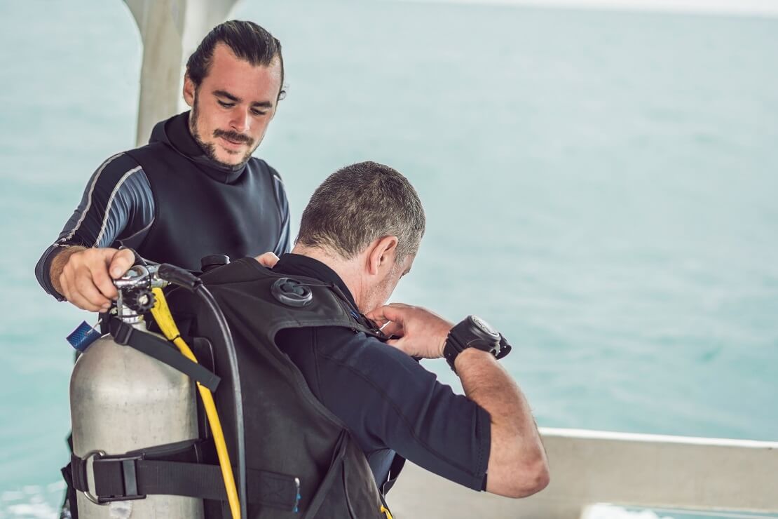 Taucher hilft seinem Partner auf einem Boot die Tauchausrüstung anzuziehen