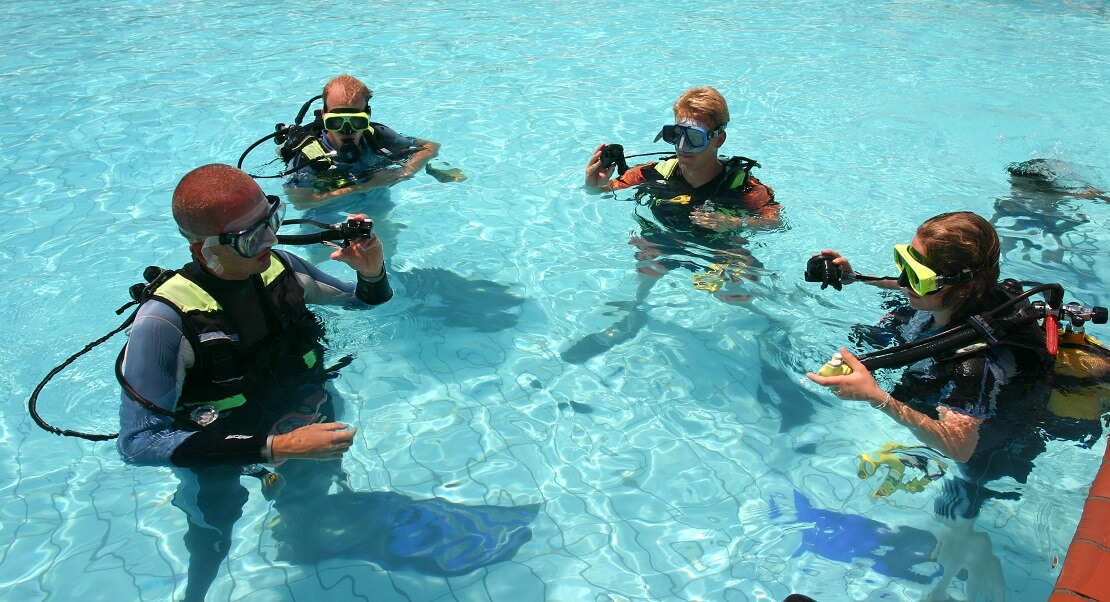 Taucherlehrer erklärt seinen Schülern im Pool die Tauchaustüstung