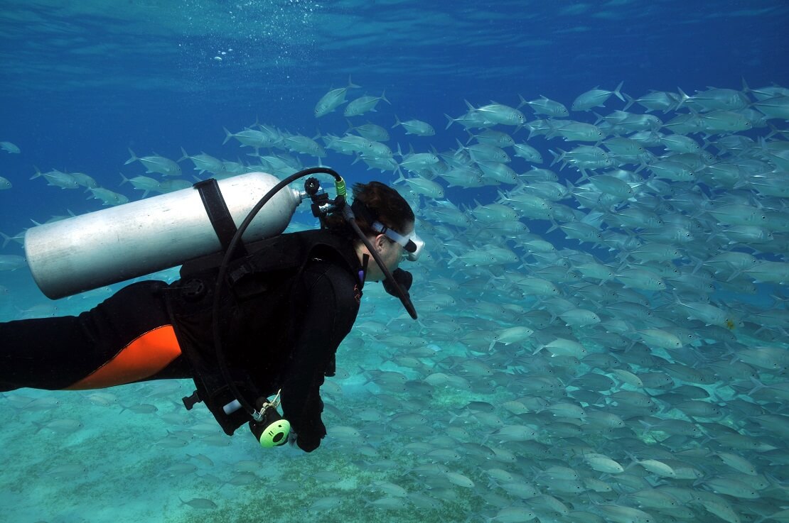 Taucherin unter Wasser mit Tauchausrüstung im Hintergrund schwimmen Fische