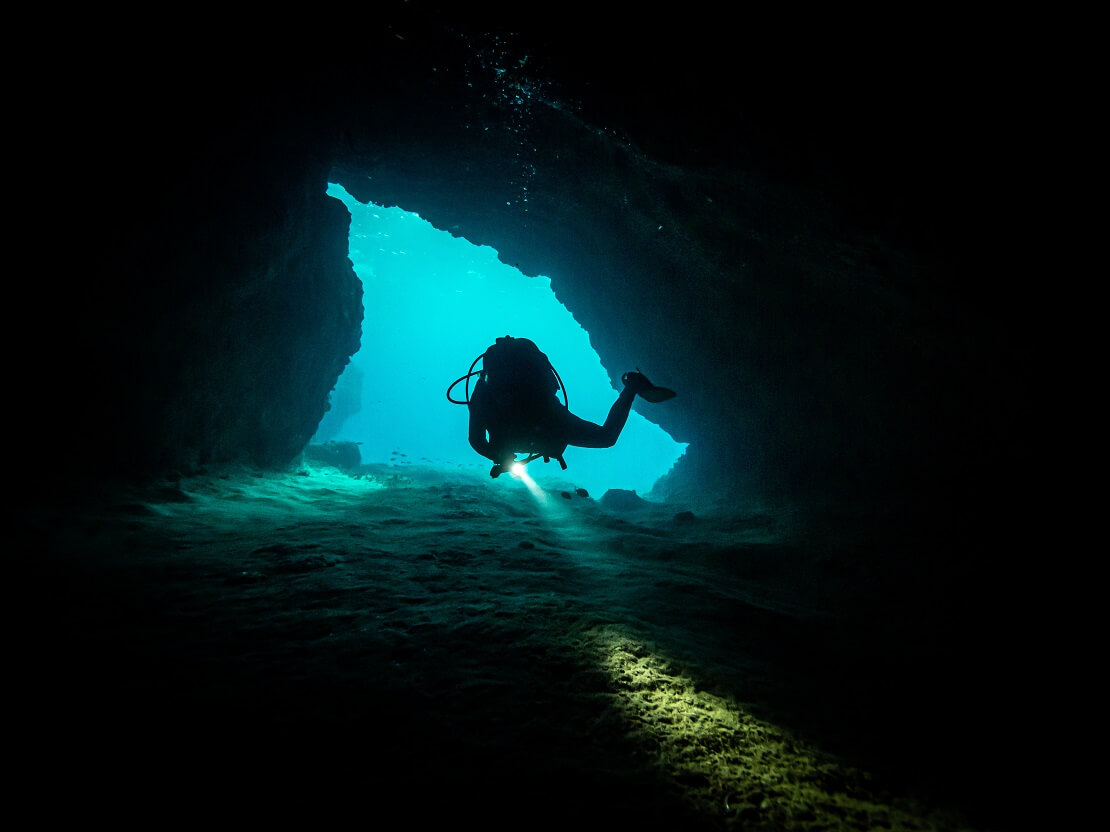 Taucher schwimmt durch schmalen Tunnel unter Wasser