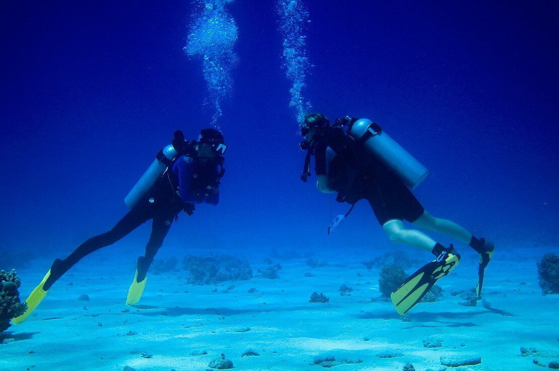 Zwei Taucher am Meeresgrund im blauen Meer gucken sich gegenseitig an