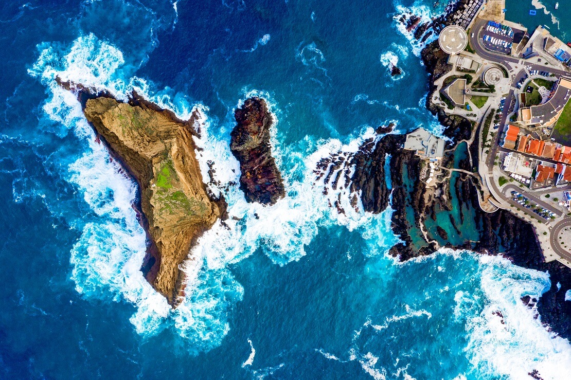 Luftbild von Madeira in der Mitte sind Felsen und die Stadt umgeben von türkisem Meer