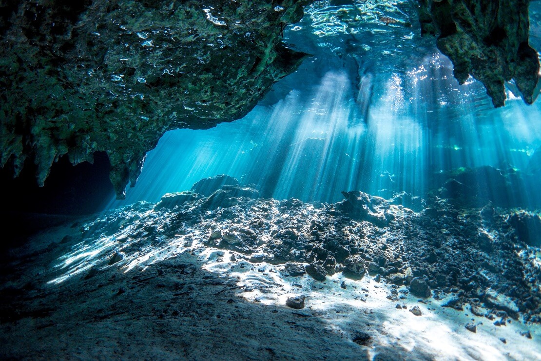 In einer Höhle fallen Sonnenstrahlen in das klare Wasser