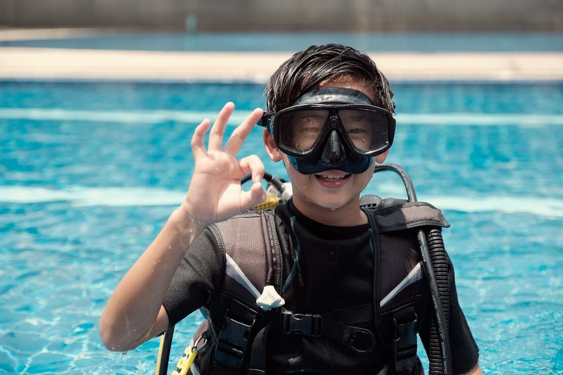 Junge steht mit Tauchausrüstung im Wasser