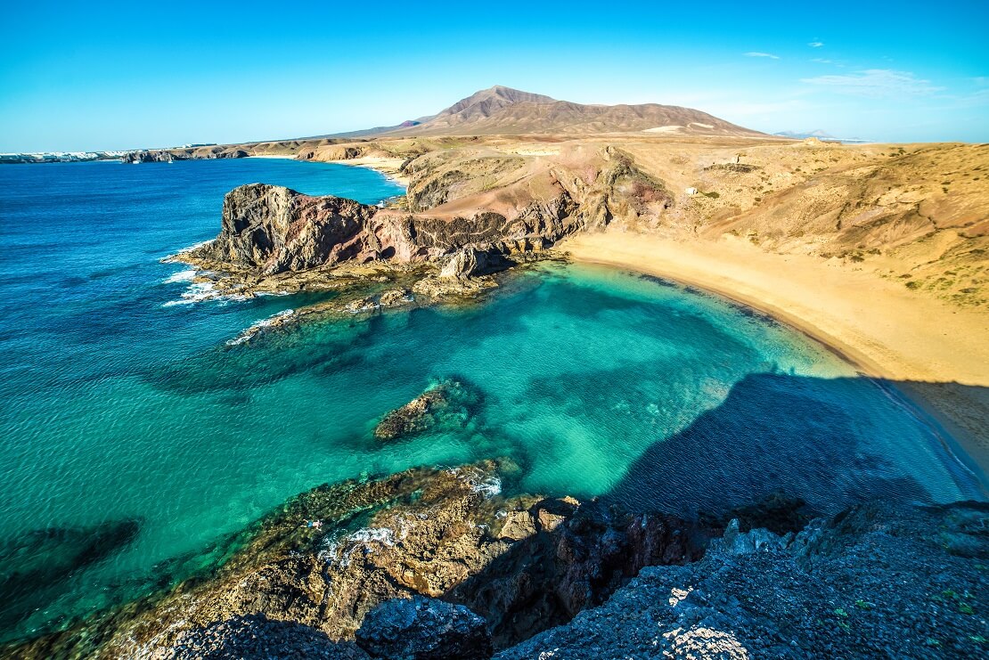 Küste von Lanzarote bei Sonnenschein im Hintergrund sind Berge