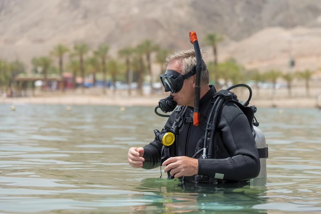 Älterer Herr steigt mit Tauchausrüstung aus dem Wasser aus