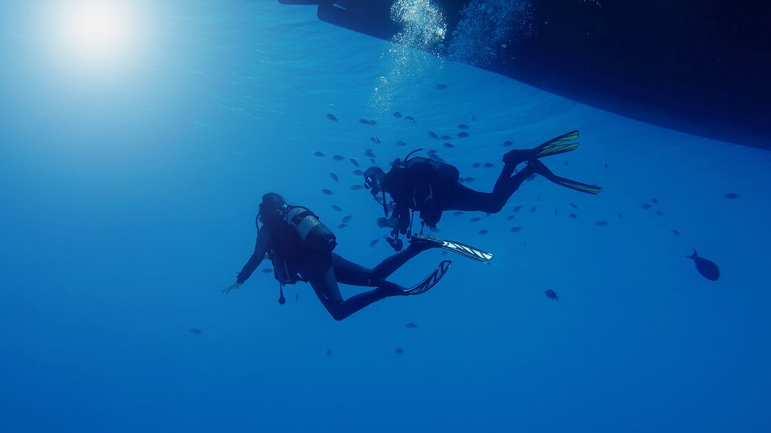 Taucher tauchen unter einem Boot um sie schwimmen Fische