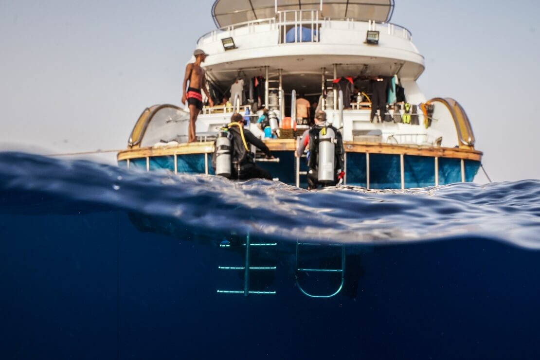 Taucher steigen die Leiter von einem Boot ab und Tauchen in das Wasser ein