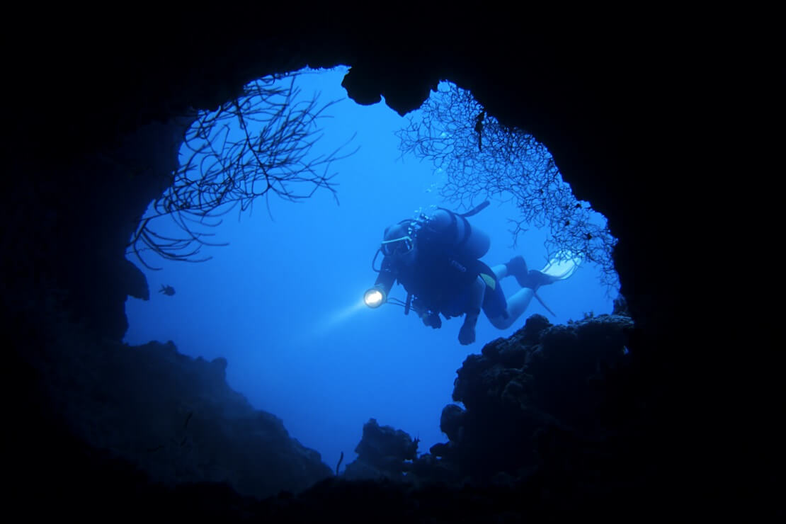 Tauch schwimmt vor einer Höhle mit einer Tauchlampe in der Hand