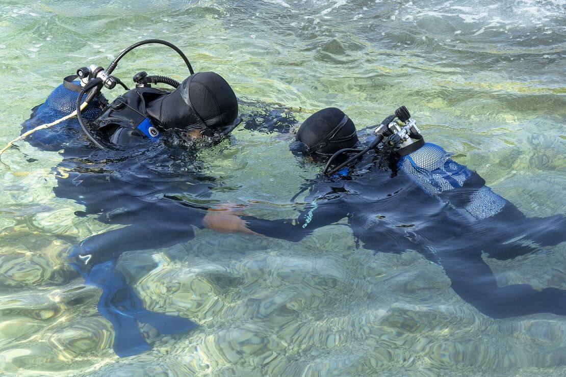 Tauchlehrer hält Kind an den Händen und taucht unter Wasser