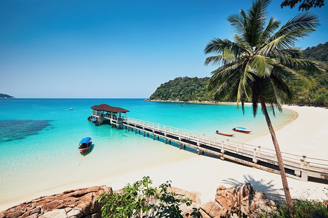 türkisblaues Wasser vor weißem Sandstrand und blauem Himmel