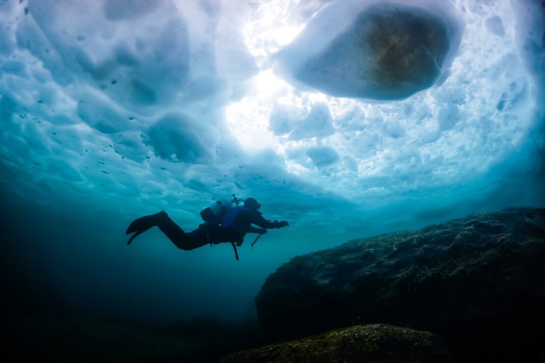 Taucher schwimmt unter einer Eisschicht