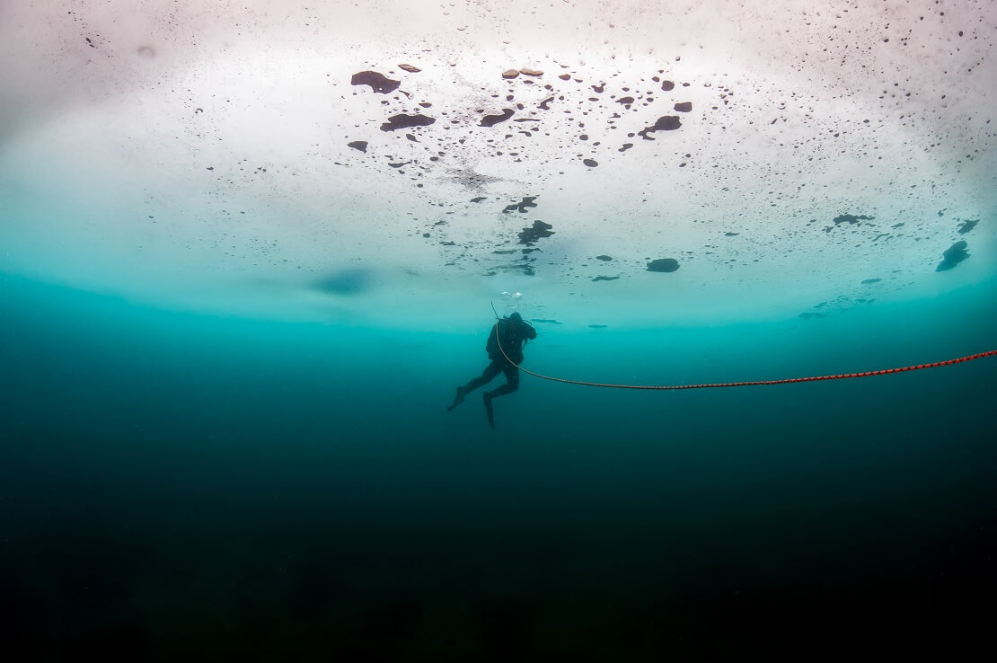 Taucher schwimmt an einem Seil entlang an einer dicken Eissicht