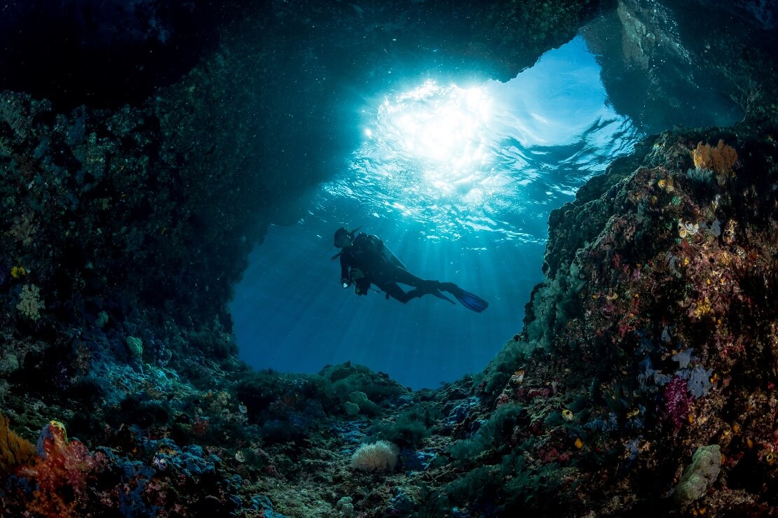 Taucher an einer Felsgrotte mit Korallen bewachsen