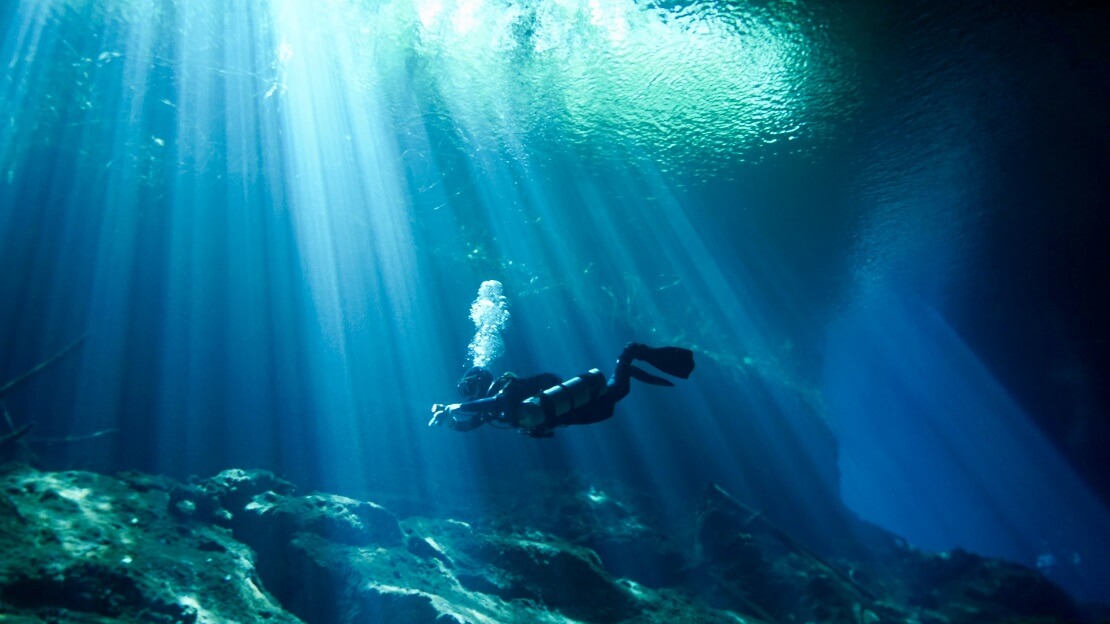 Taucher schwimmt in einer Höhle und wirft Blasen