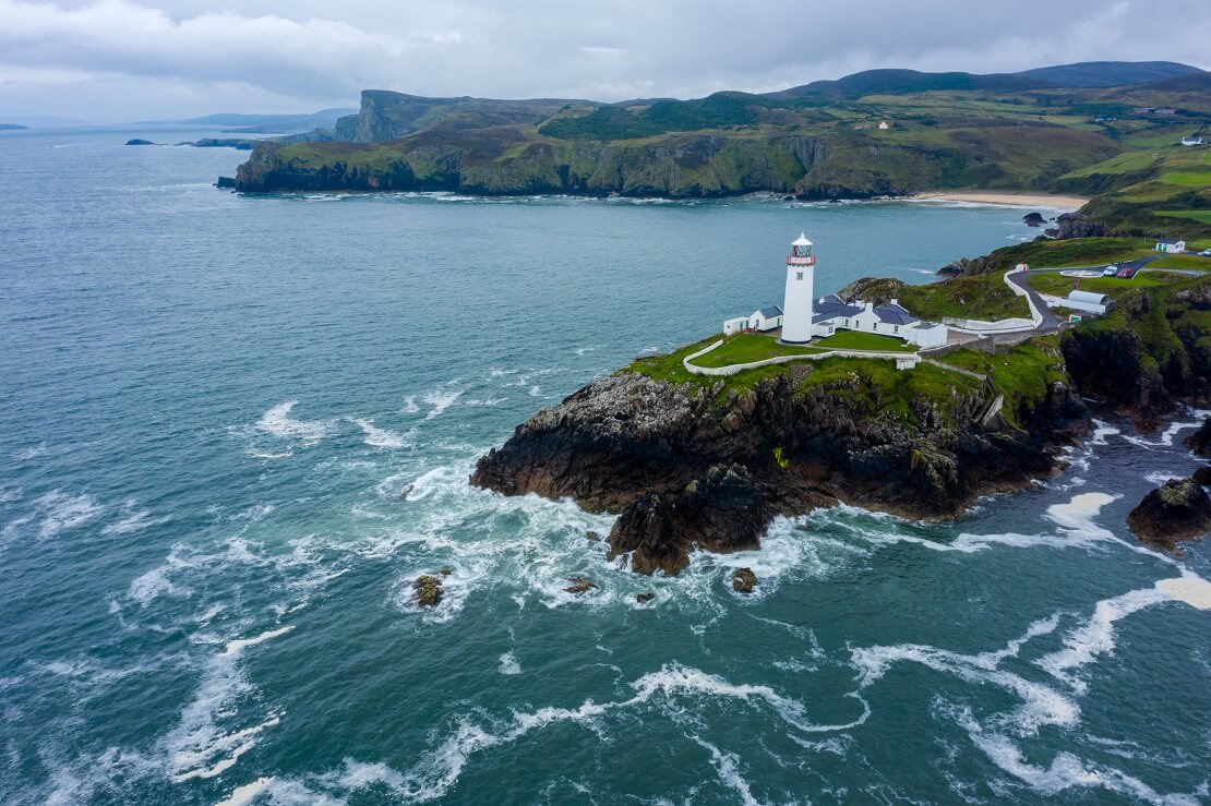 Küste von Lough Swilly mit den Leuchtturm und Bergen im Hintergrund