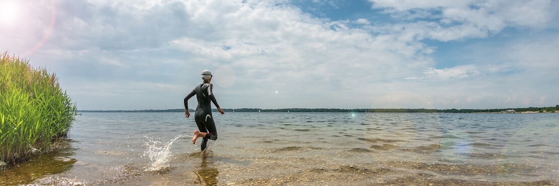 Taucherin läuft in Nassanzug ins Wasser