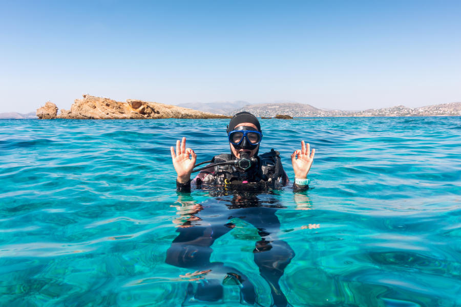 Eine Taucherin an der Meeresoberfläche gibt mit beiden Händen das OK-Zeichen